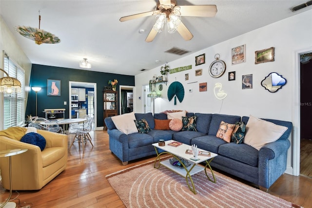 living room with a ceiling fan, visible vents, and wood finished floors