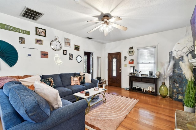 living room with a textured ceiling, wood finished floors, visible vents, and a ceiling fan