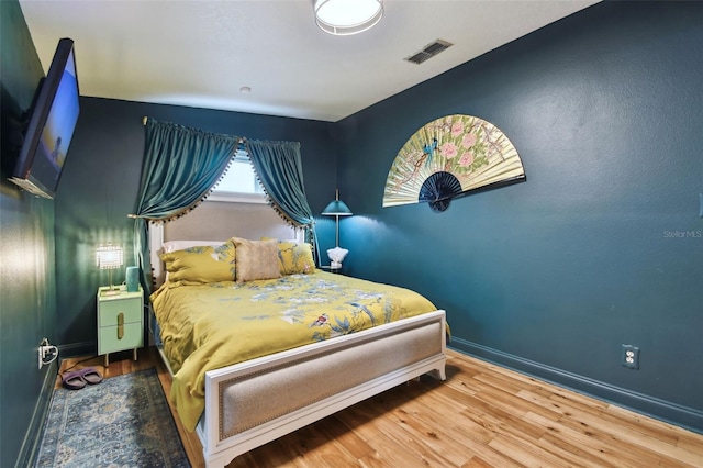 bedroom with baseboards, visible vents, and wood finished floors