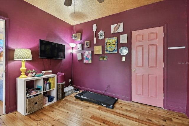 rec room with a textured ceiling, wood finished floors, a ceiling fan, and baseboards