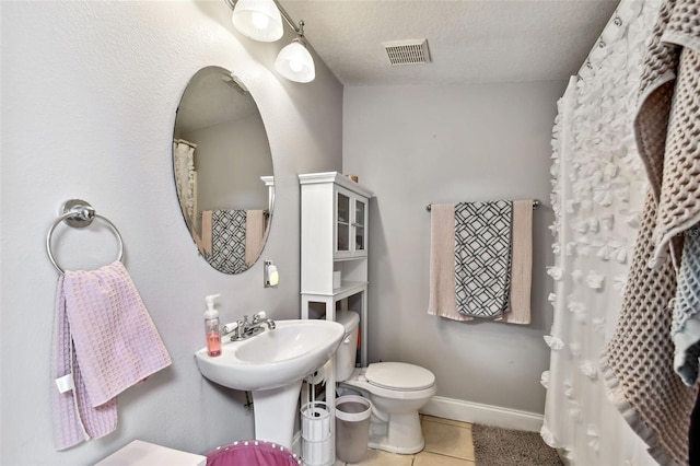 bathroom featuring visible vents, toilet, a textured ceiling, baseboards, and tile patterned floors