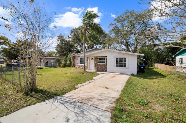 view of front of property featuring concrete driveway, a front lawn, stone siding, and fence