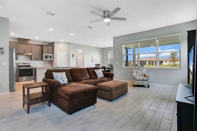 living room with baseboards, a ceiling fan, light wood-style flooring, and recessed lighting