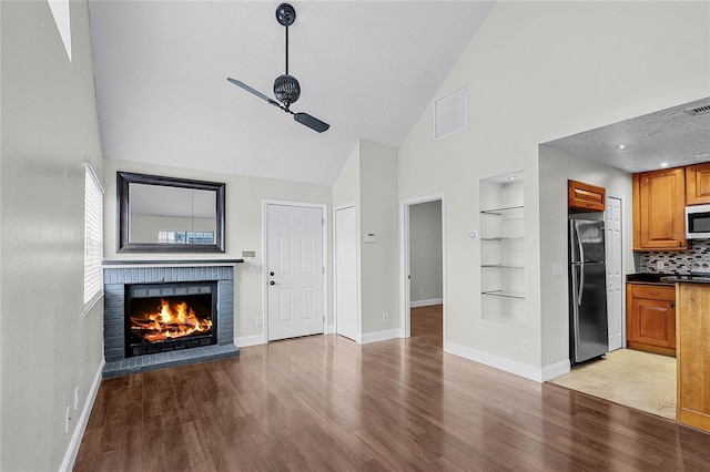 unfurnished living room featuring lofted ceiling, a fireplace, baseboards, built in features, and light wood finished floors