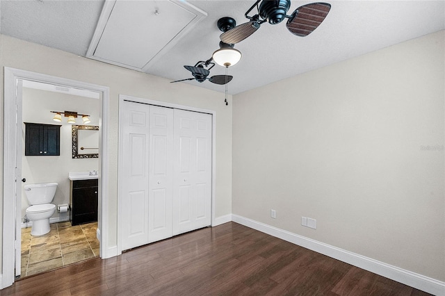 unfurnished bedroom with attic access, baseboards, connected bathroom, dark wood-style floors, and a closet