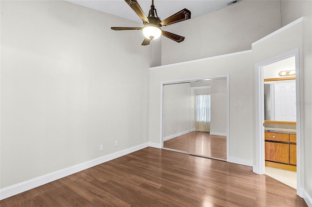 unfurnished bedroom with a closet, ceiling fan, connected bathroom, wood finished floors, and baseboards