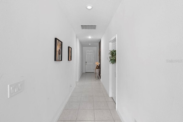 hallway with light tile patterned floors, a textured ceiling, recessed lighting, visible vents, and baseboards