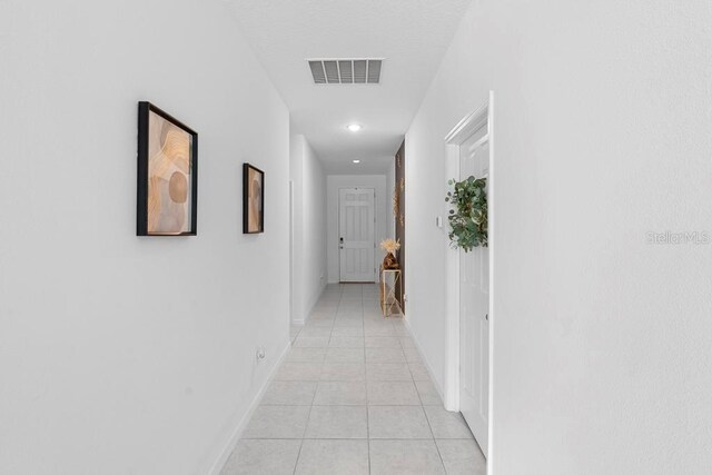 hallway featuring visible vents, baseboards, and light tile patterned floors