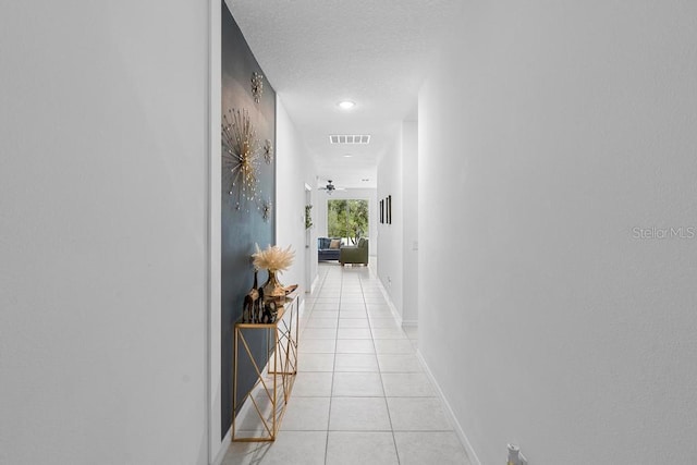 hallway featuring light tile patterned floors, a textured ceiling, visible vents, and baseboards