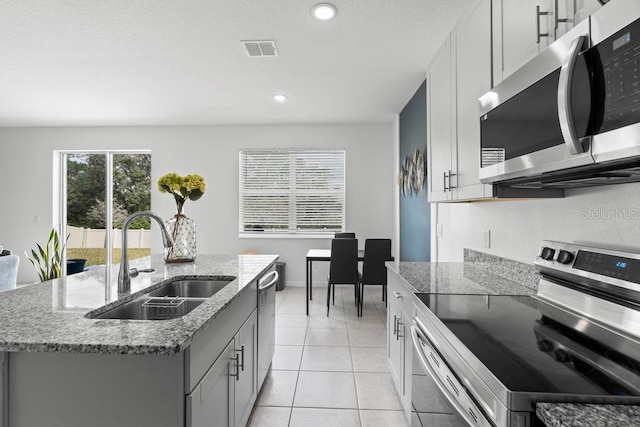 kitchen featuring light stone counters, light tile patterned floors, stainless steel appliances, visible vents, and a sink