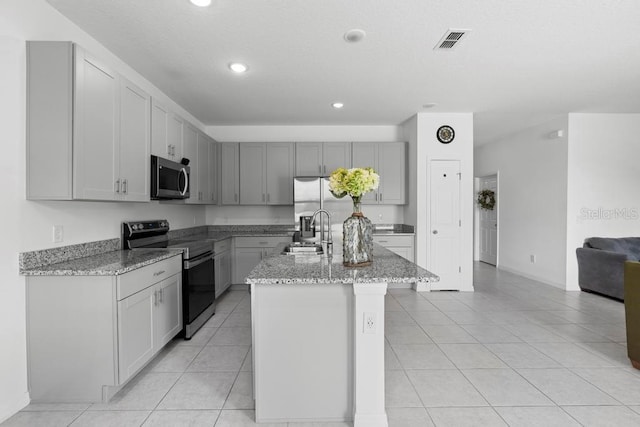 kitchen with a kitchen island with sink, stainless steel appliances, a sink, visible vents, and light stone countertops