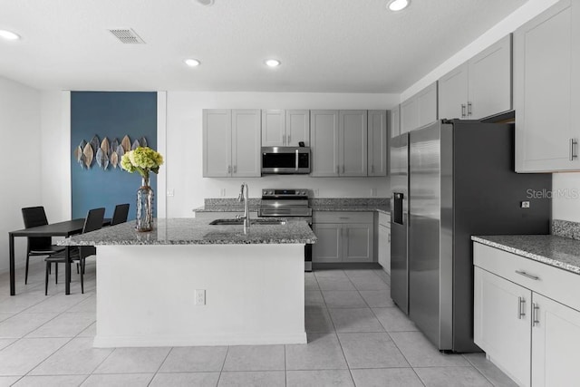 kitchen with visible vents, light stone countertops, gray cabinets, stainless steel appliances, and a sink