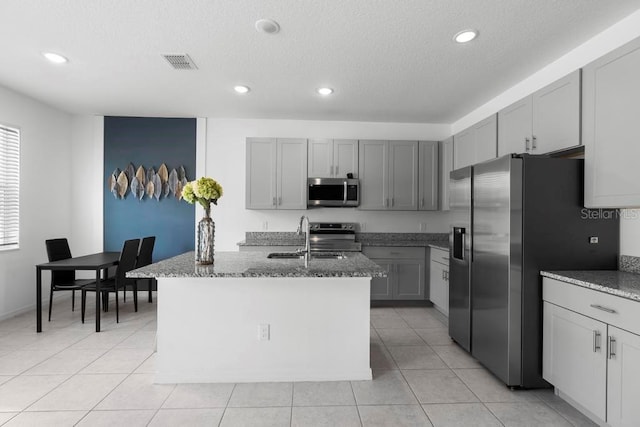 kitchen featuring light tile patterned floors, stone counters, a sink, visible vents, and appliances with stainless steel finishes