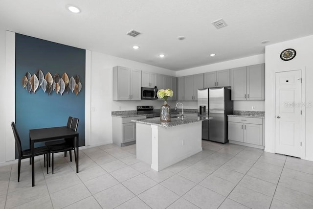 kitchen featuring light stone counters, a center island with sink, visible vents, gray cabinetry, and appliances with stainless steel finishes