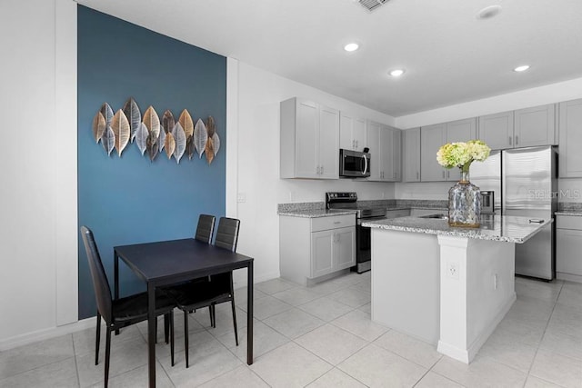 kitchen with stainless steel appliances, gray cabinets, a center island with sink, and light stone countertops