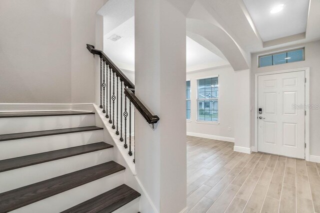 foyer entrance with visible vents, baseboards, wood finished floors, arched walkways, and a raised ceiling