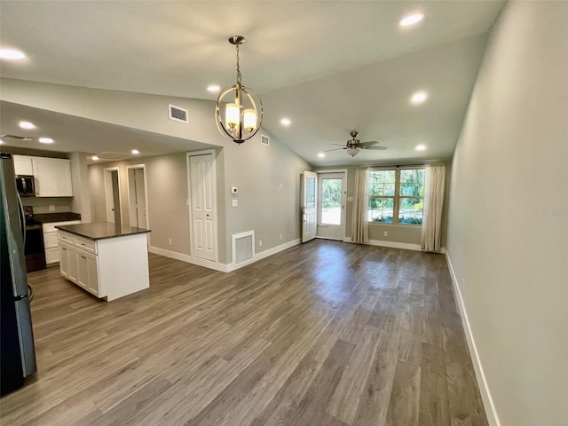 interior space with wood finished floors, white cabinets, vaulted ceiling, appliances with stainless steel finishes, and dark countertops