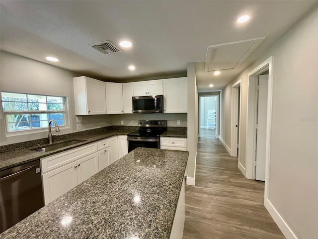 kitchen featuring stainless steel appliances, visible vents, white cabinetry, a sink, and dark stone countertops