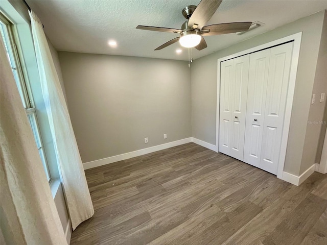 unfurnished bedroom with a textured ceiling, ceiling fan, wood finished floors, baseboards, and a closet