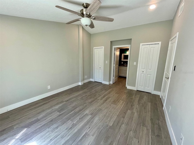 unfurnished bedroom with baseboards, wood finished floors, a ceiling fan, and multiple closets