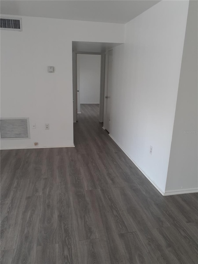 spare room with baseboards, visible vents, and dark wood-style flooring