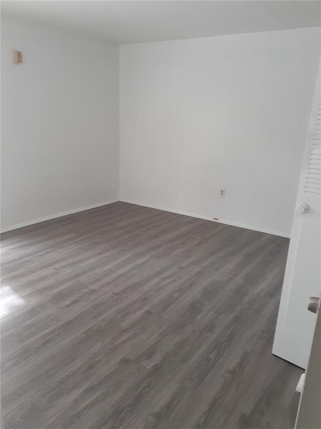 unfurnished room with baseboards and dark wood-type flooring