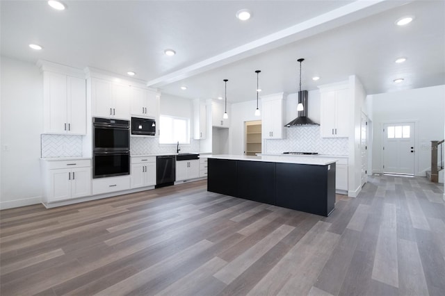 kitchen featuring light countertops, hanging light fixtures, white cabinetry, wall chimney range hood, and black appliances