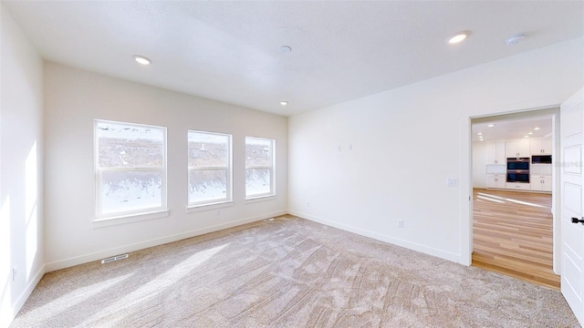 spare room with recessed lighting, light carpet, visible vents, and baseboards