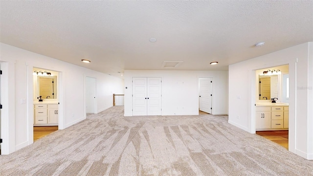 unfurnished bedroom featuring light carpet, ensuite bath, baseboards, and a textured ceiling