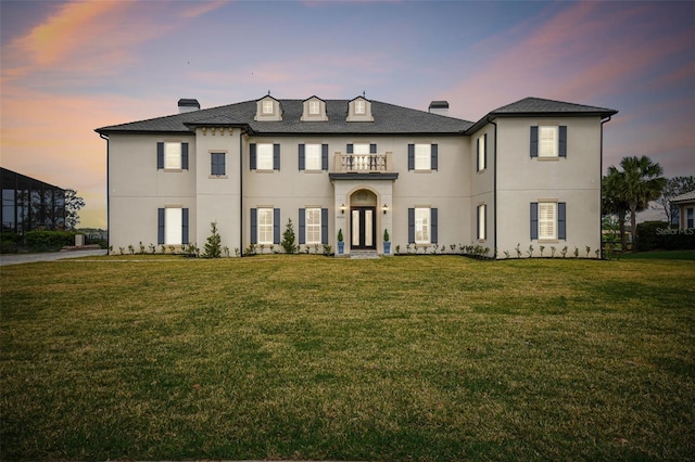 view of front of property featuring a front yard, a chimney, a balcony, and stucco siding