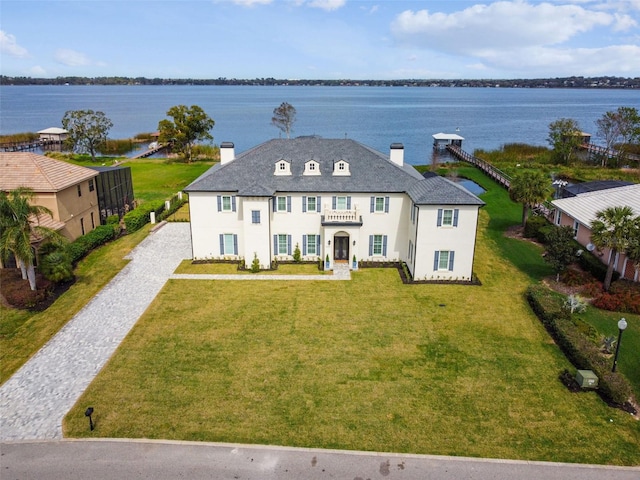 french provincial home with a water view, a chimney, a front lawn, and stucco siding