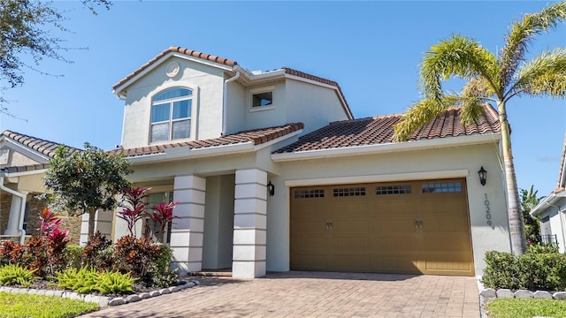 mediterranean / spanish-style home featuring a garage, a tile roof, decorative driveway, and stucco siding