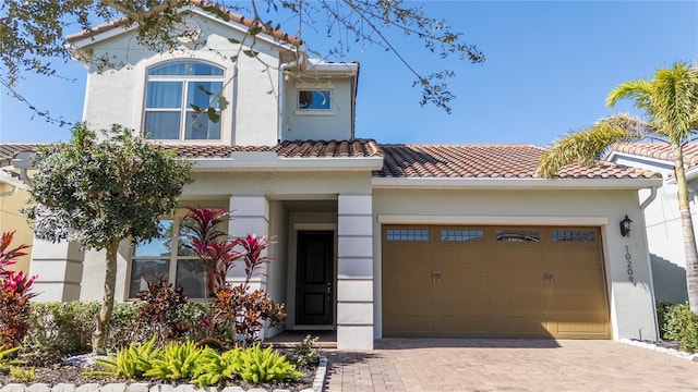 mediterranean / spanish-style home with decorative driveway, an attached garage, a tile roof, and stucco siding