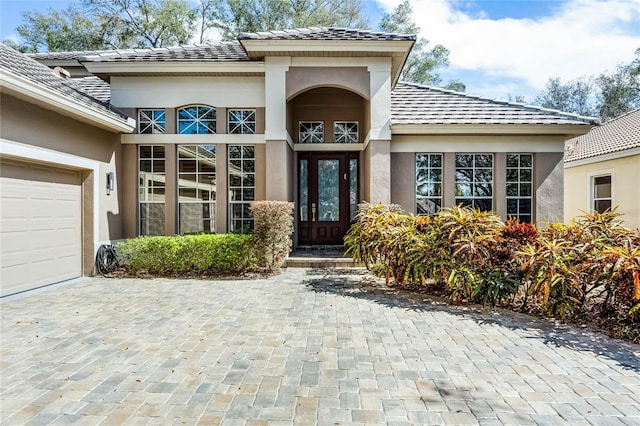 doorway to property featuring a tile roof, an attached garage, and stucco siding