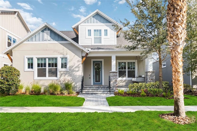 craftsman-style house with roof with shingles, a porch, board and batten siding, and a front yard