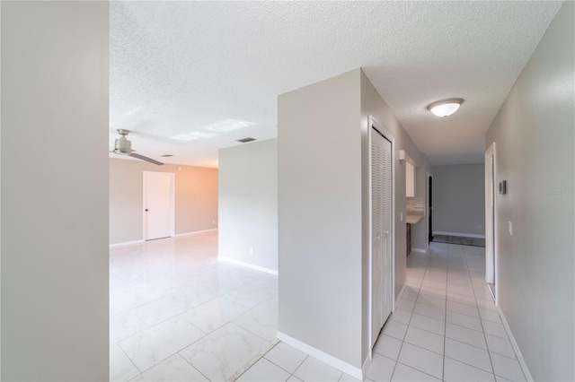 hallway with marble finish floor, visible vents, baseboards, and a textured ceiling