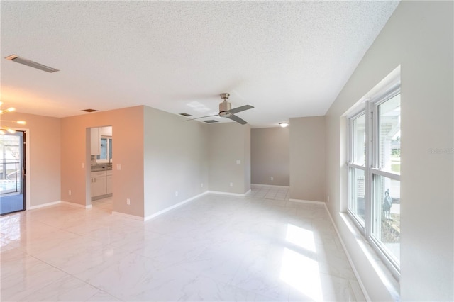 spare room with a textured ceiling, ceiling fan with notable chandelier, visible vents, baseboards, and marble finish floor