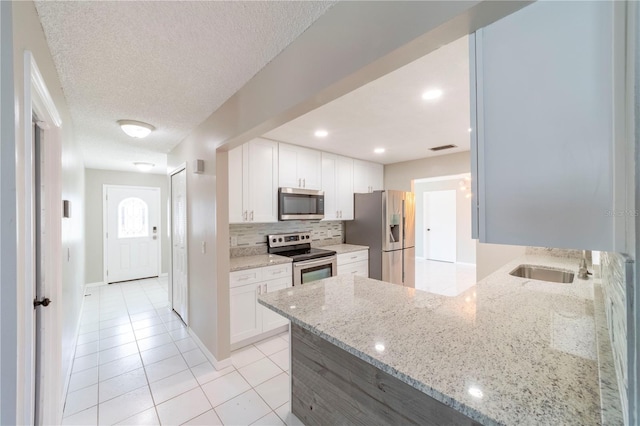 kitchen featuring light stone counters, stainless steel appliances, a sink, white cabinets, and backsplash