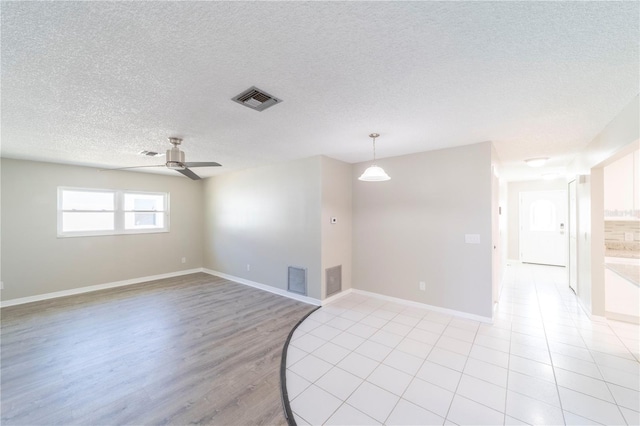 spare room with baseboards, ceiling fan, visible vents, and a textured ceiling