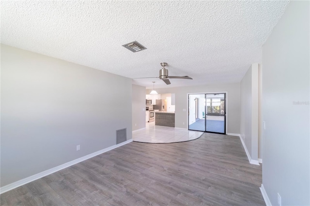 empty room with a textured ceiling, wood finished floors, visible vents, and baseboards