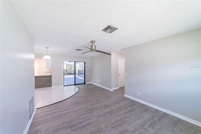 empty room with baseboards, visible vents, ceiling fan, wood finished floors, and a textured ceiling