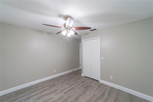 unfurnished bedroom featuring a textured ceiling, visible vents, light wood-style floors, baseboards, and a closet