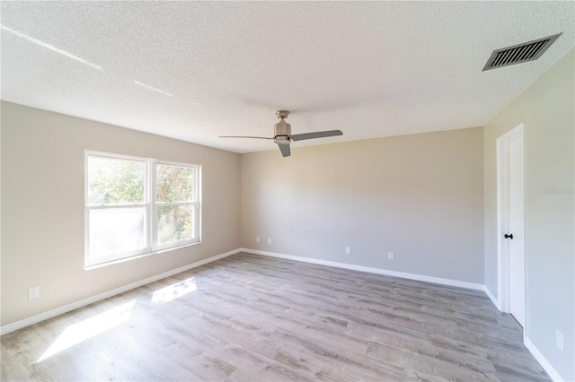 spare room with a textured ceiling, light wood-style flooring, a ceiling fan, visible vents, and baseboards