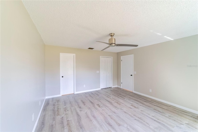 empty room with light wood-style floors, visible vents, baseboards, and a textured ceiling