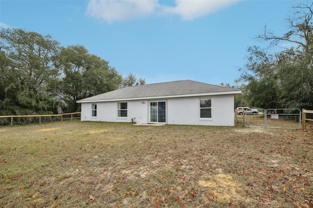 rear view of property featuring a lawn, fence, a gate, and stucco siding