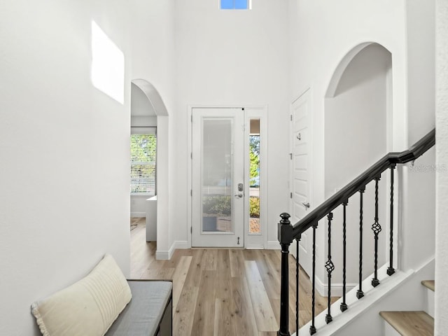 foyer with a towering ceiling, light wood-style floors, stairway, and arched walkways