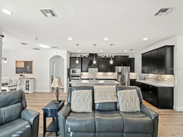 living room with arched walkways, baseboards, visible vents, and light wood-style floors