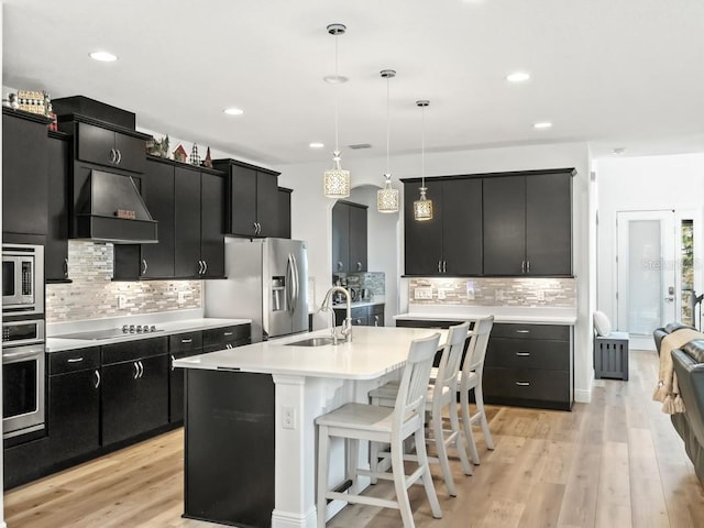 kitchen with dark cabinets, stainless steel appliances, a sink, light countertops, and decorative light fixtures