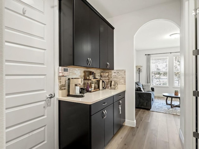 bar with arched walkways, light wood-style floors, baseboards, and decorative backsplash