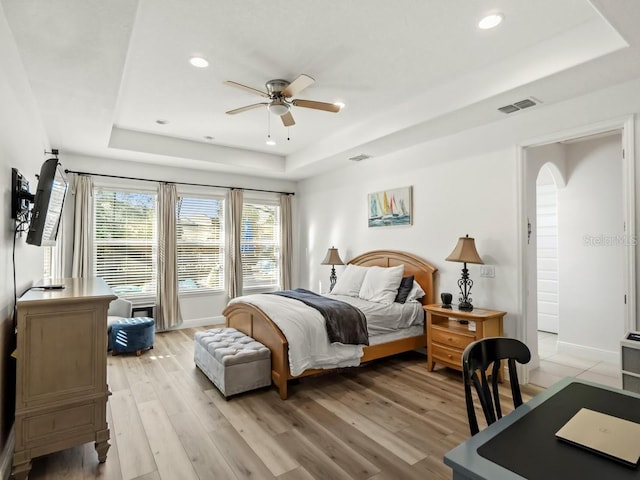 bedroom with light wood-style floors, visible vents, and a raised ceiling